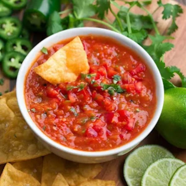 Don Jose Mexican Restaurant's fresh salsa with a tortilla chip, surrounded by limes, cilantro, and jalapeños.