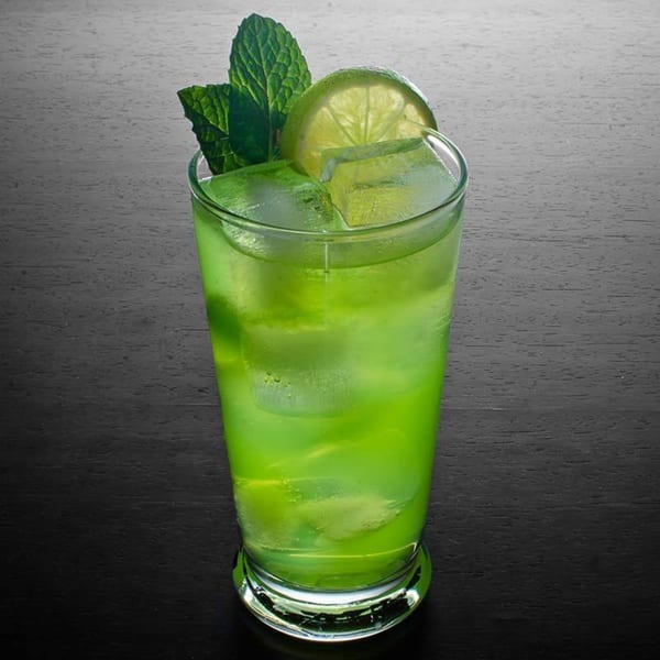 Bright green cocktail with ice, a lime slice, and mint leaves on a dark wooden surface.