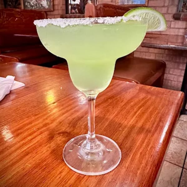 A Don Jose Mexican Restaurant margarita with a salted rim and lime wedge on a wooden table.